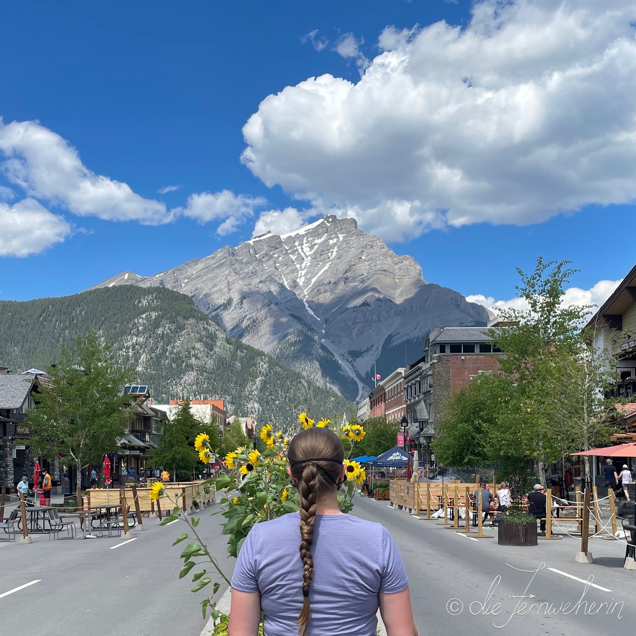 A woman stands in the middle of Banff Avenue looking towards downtown Banff.