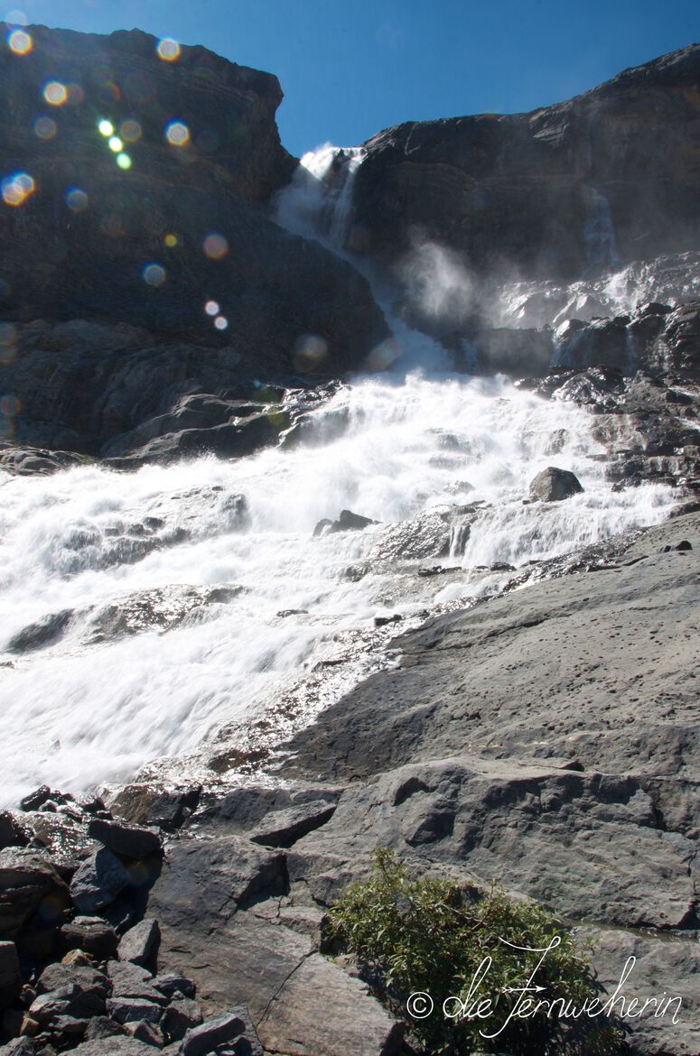 Bow Glacier Falls rushes over rocks in Banff National Park as the spray sparkles in the sunlight.