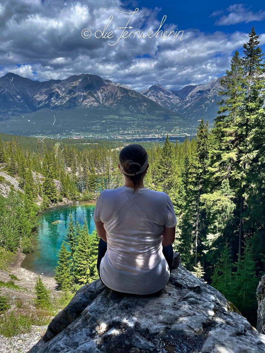 A woman sits on a rock overlooking brilliant green Grassi Lakes in Kananaskis Country, Alberta.