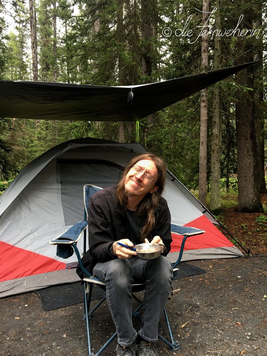 A man sits in a camp chair in front of a tent in Lake Louise Campground.