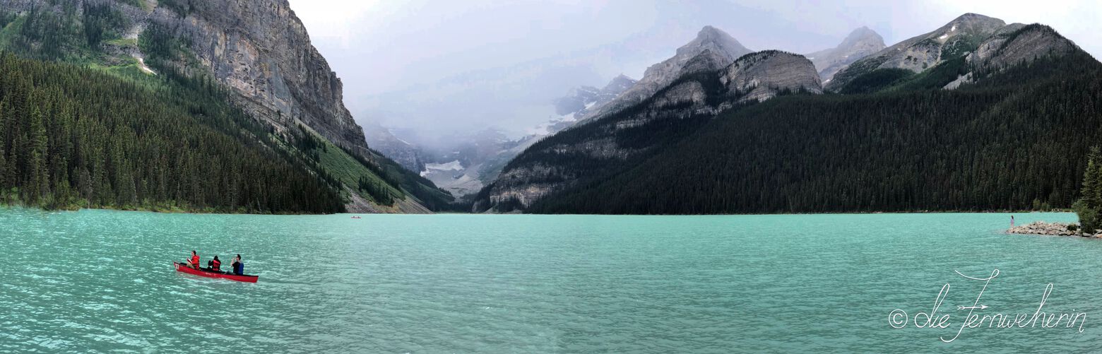 Three people paddle an iconic red canoe on a rainy day at Lake Louise in Banff National Park.