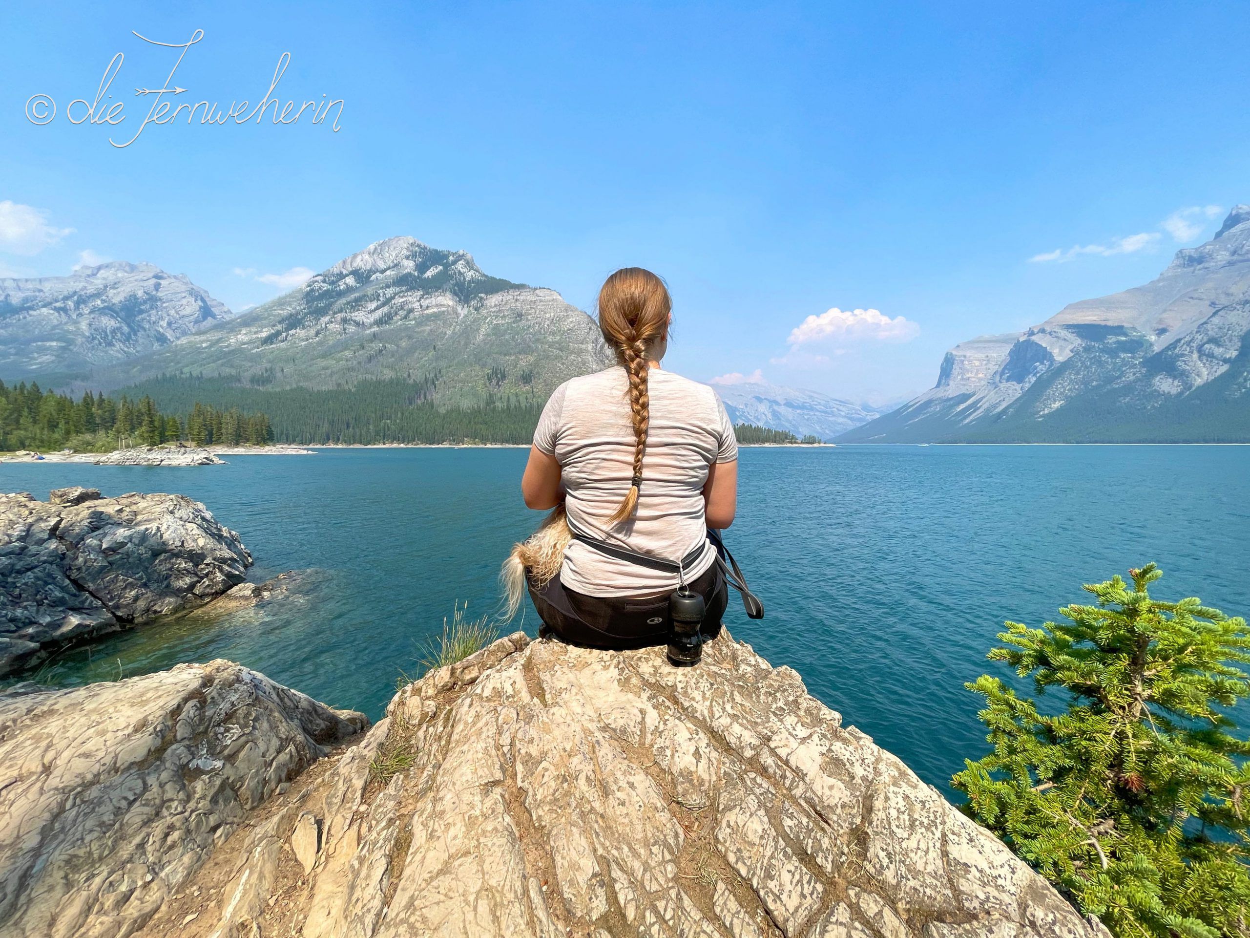 A woman sits on a rock looking out over Lake Minnewanka in Banff National Park.