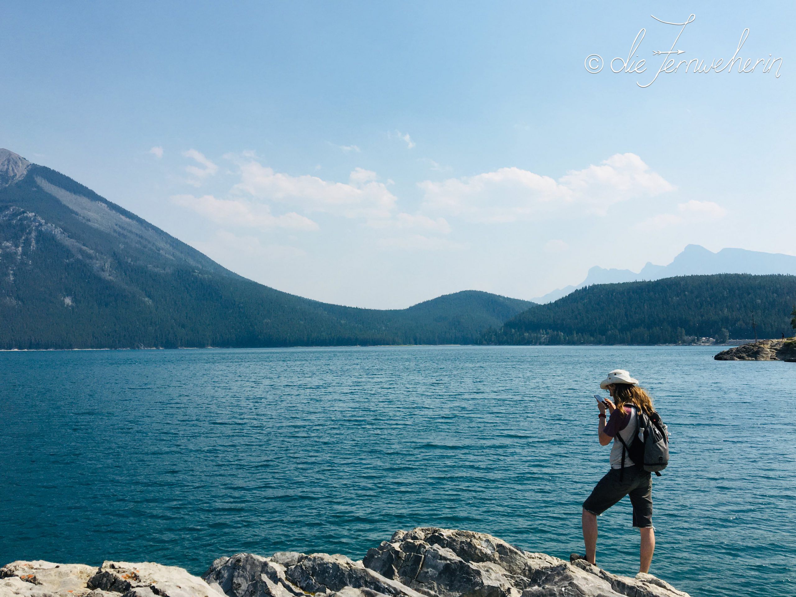 A man stands on the rocky shore around Lake Minnewanka in Banff National Park.