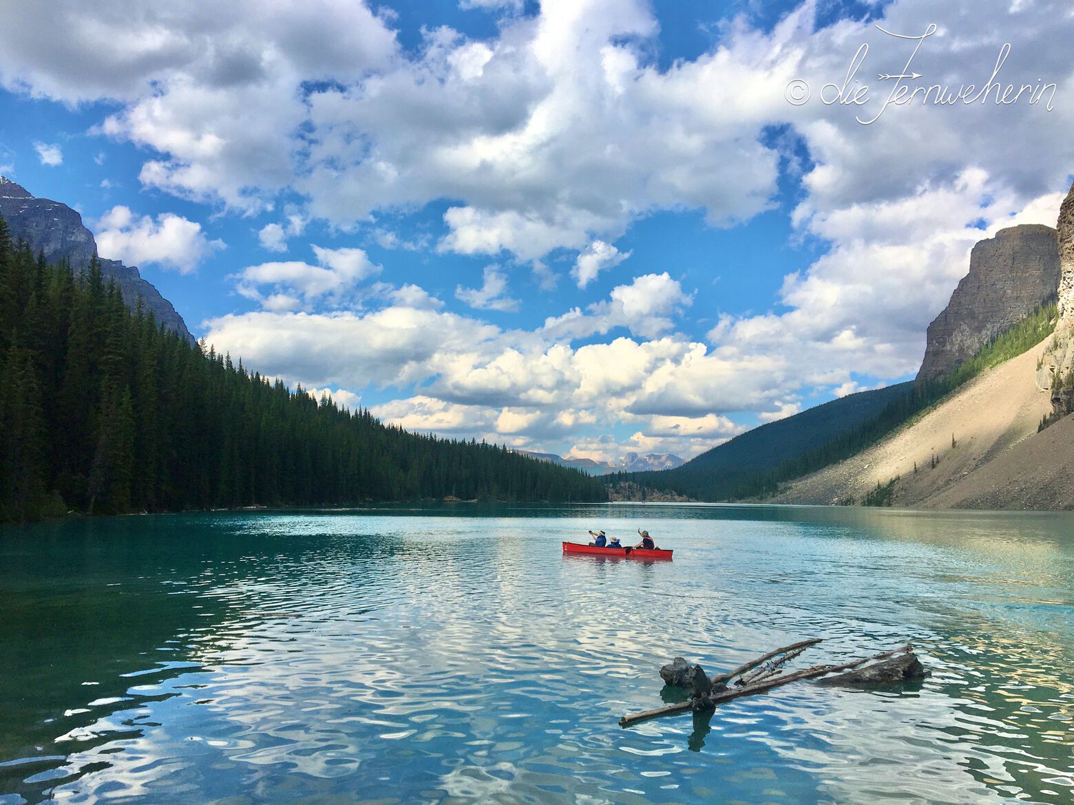 A red canoe floats in the middle of turquoise-blue Moraine Lake in Banff National Park.