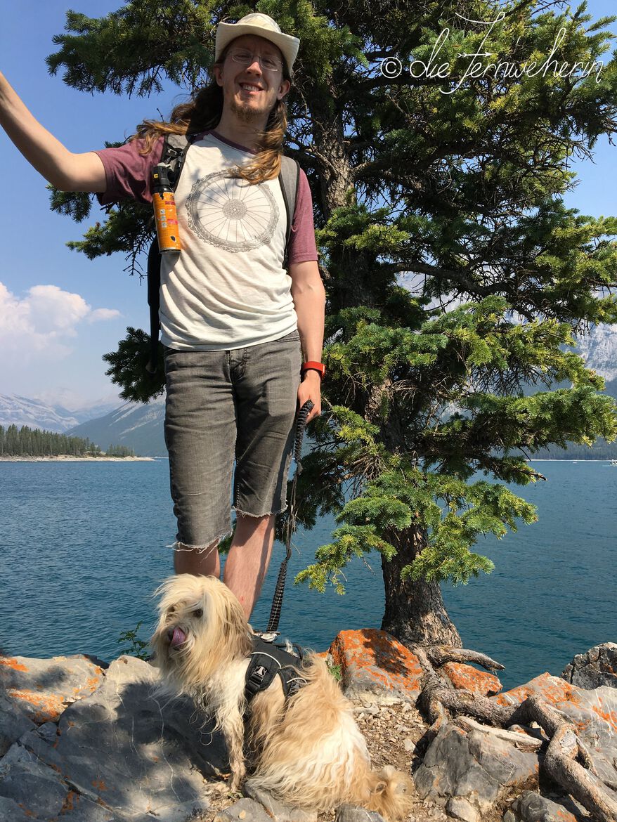 A man & a dog pose in front of Lake Minnewanka in Banff National Park.