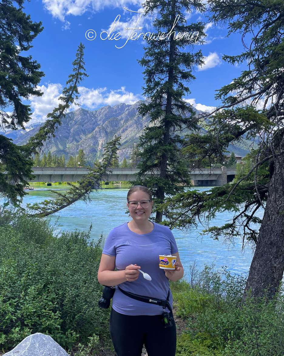 A woman eating ice cream in front of the Bow River in the town of Banff.