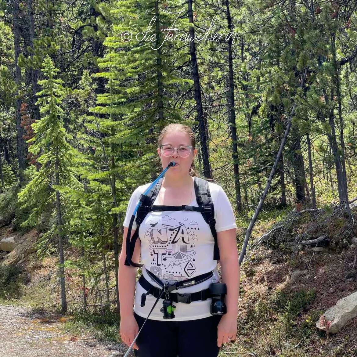 A hiker poses with her hydration backpack on a forested trail.