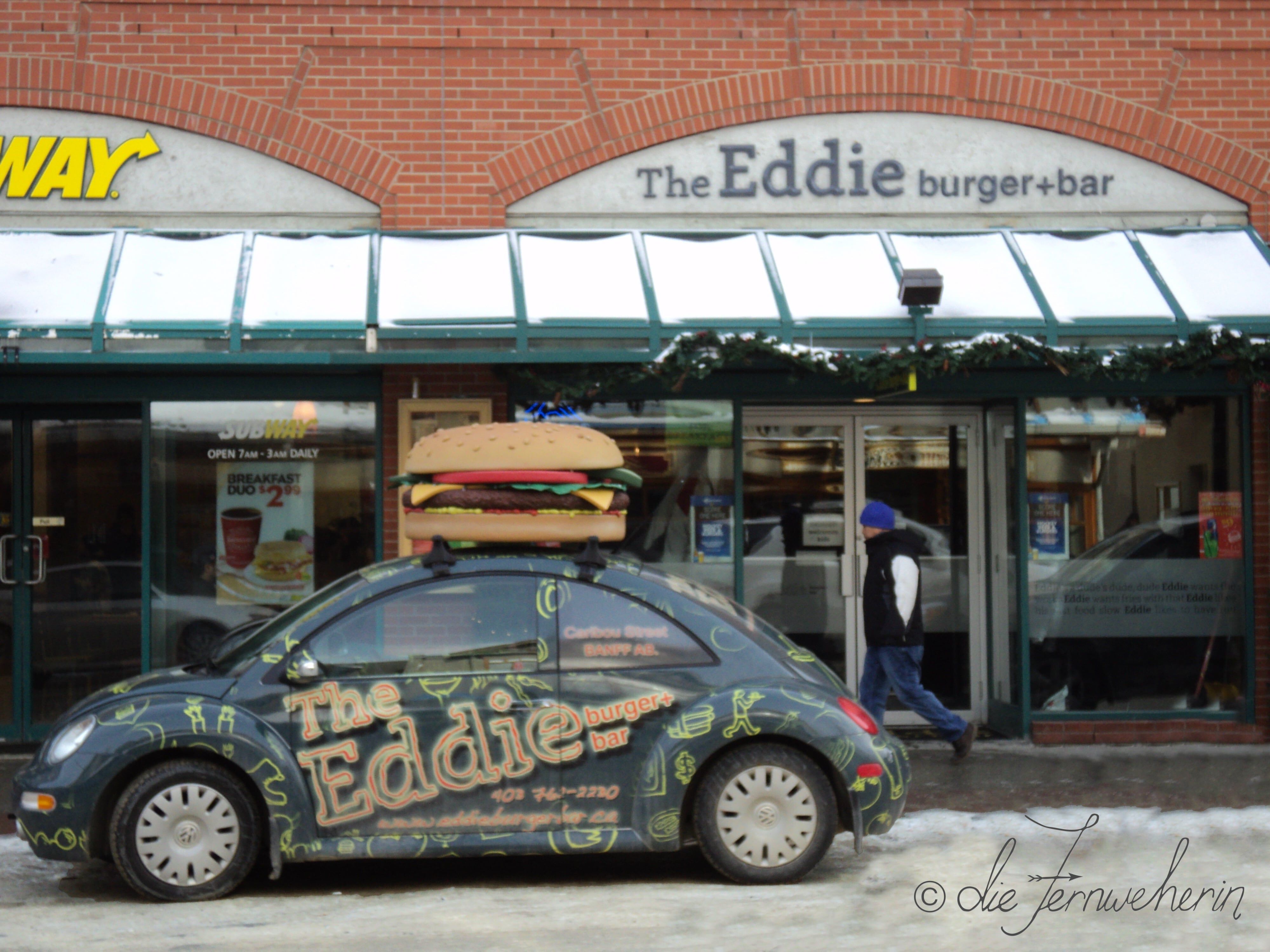 Exterior view of The Eddie Burger + Bar, a restaurant in the town of Banff, and the Eddie Mobile, a green VW Bug with a giant burger on the roof.