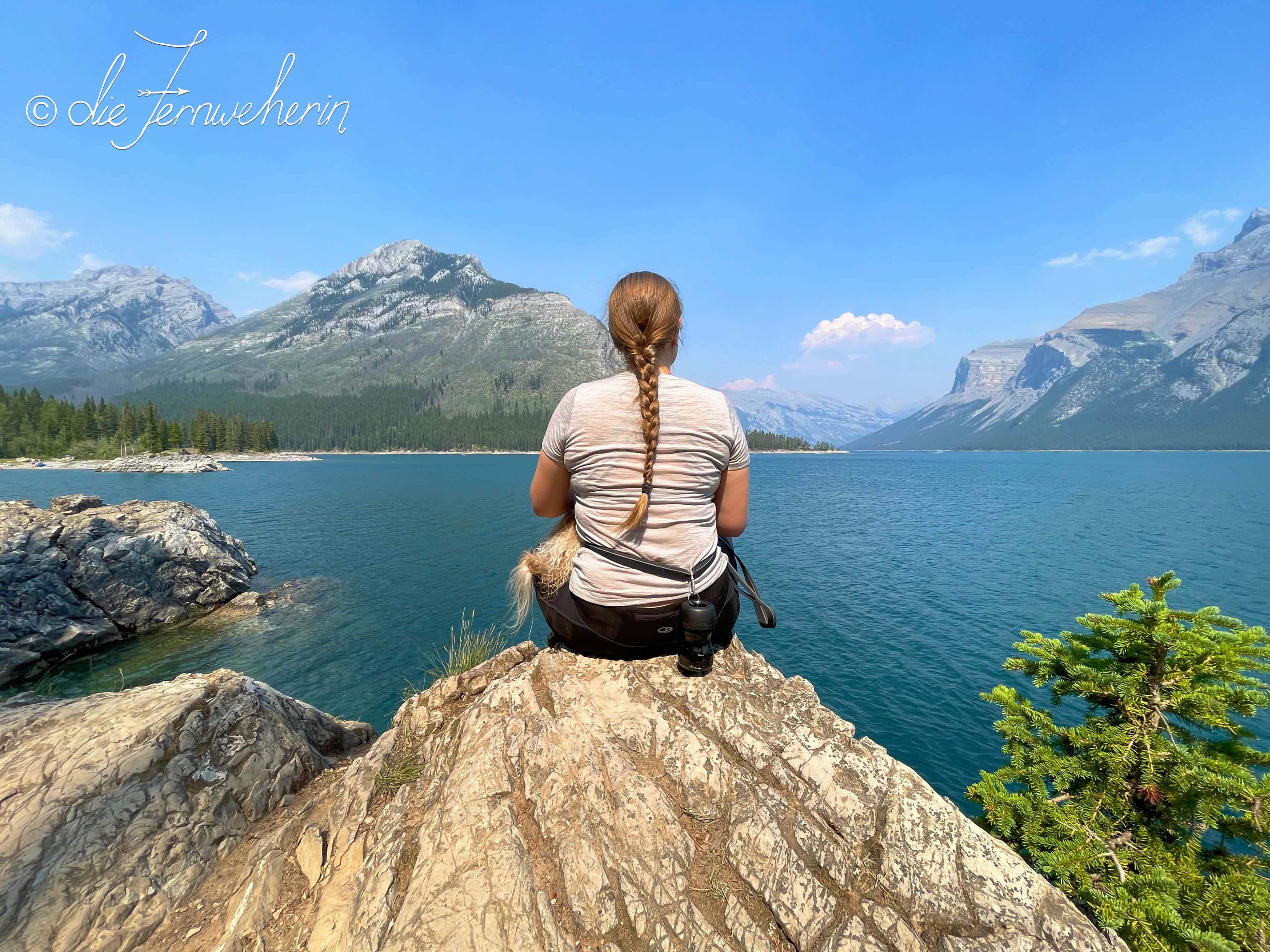 A woman sits on a rock overlooking beautiful blue Lake Minnewanka in Banff National Park.