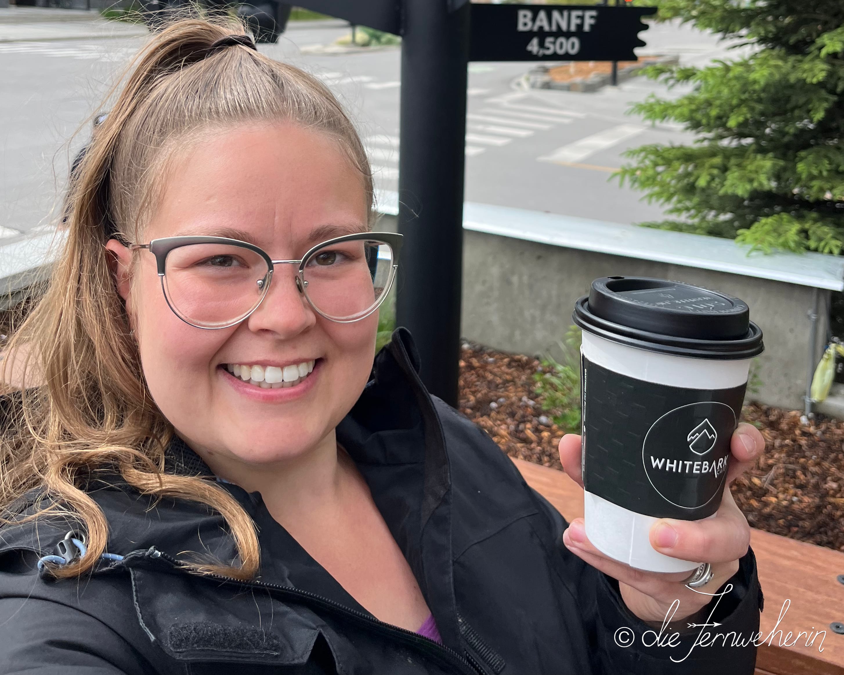 Jenn posing with a to-go hot chocolate on the patio outside of Whitebark Café in downtown Banff.